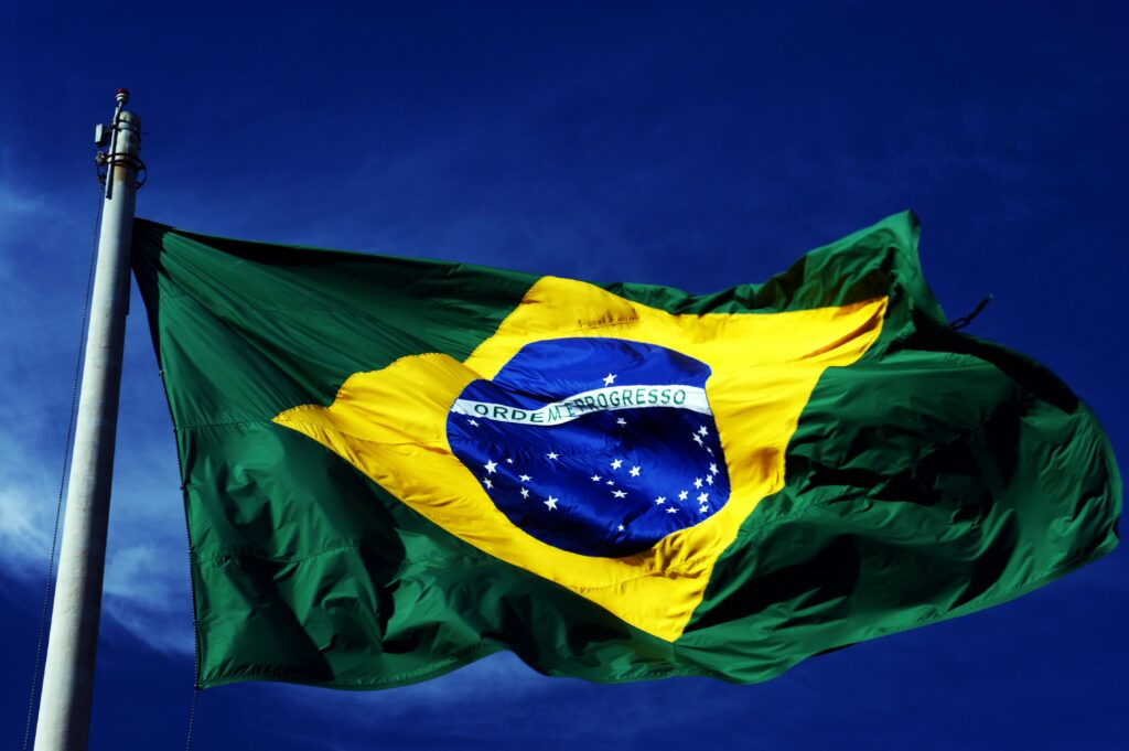 A dynamic shot of the Brazilian flag waving on a flagpole with a clear blue sky background.