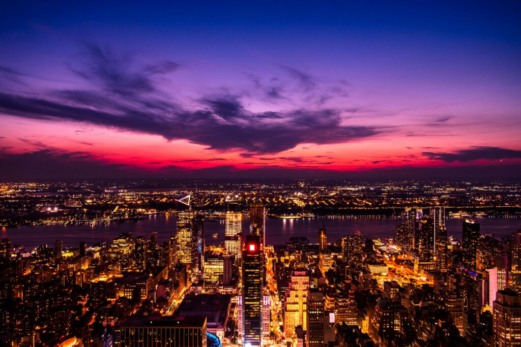 Stunning aerial view of New York City skyline against a dramatic sunset sky with vibrant lights.